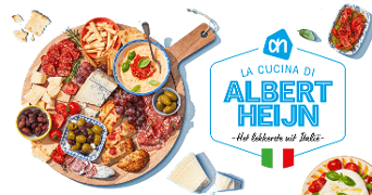 Ronde houten borrelplank met Italiaanse specialiteiten zoals verschillende kazen, worst, olijven, druiven, tomaat, hummus en brood, gepresenteerd naast een bord met het logo van Albert Heijn en de tekst "La cucina di Albert Heijn - Het lekkerste uit Italië" met Italiaanse vlag.