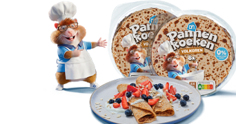 Twee verpakkingen AH Pannenkoeken volkoren met een cartoonhamster in bakkerstenue, naast een bord met opgerolde pannenkoeken, aardbeien, blauwe bessen en kokosrasp.
