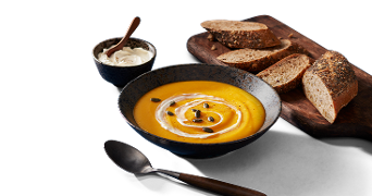Bord met pompoensoep en broodplank met gesneden stokbrood erop
