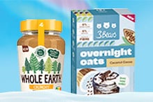 Pot Whole Earth crunchy pindakaas en doos 3Bears overnight oats kokos-cacao naast elkaar op een blauwe achtergrond.