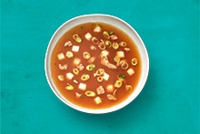 Kom met heldere bouillonsoep, blokjes tofu en groente.