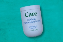 Potje met Care calcium, magnesium en zink tabletten van Albert Heijn op een groene achtergrond.