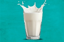 Glas melk met spetters tegen een turquoise achtergrond.