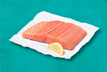 Verse zalmfilet met een schijfje citroen op een witte ondergrond.