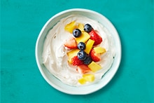Yoghurt met aardbeien, ananas en bosbessen in een schaaltje op een blauwe achtergrond.