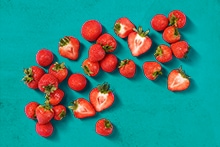 Verse aardbeien, hele en gehalveerde, verspreid op een turquoise ondergrond