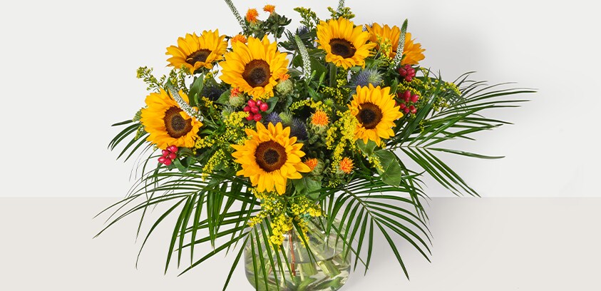 Boeket met gele zonnebloemen en groene bladeren in een glazen vaas