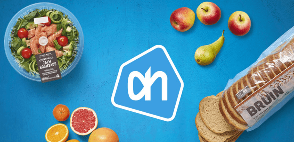 Salade met zalm roomsaus, verschillende soorten fruit, gesneden bruinbrood en het Albert Heijn-logo op een blauwe achtergrond.