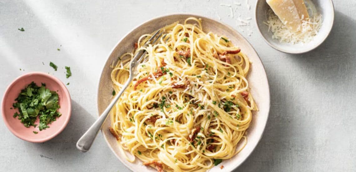 Spaghetti carbonara geserveerd op een bord, met geraspte kaas en verse peterselie erbij.