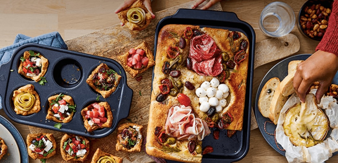 Diverse borrelhapjes met focaccia, hartige muffins, stokbrood en een gesmolten kaasdip op een houten tafel.