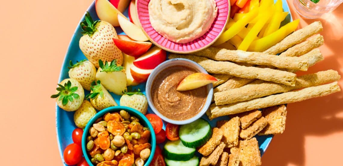 Borrelplank met witte aardbeien, appelpartjes, komkommer, snoeptomaatjes, gegrilde groentesticks, hummus, notendip, paprika reepjes, toastjes en een mix van geroosterde kikkererwten en groentechips.