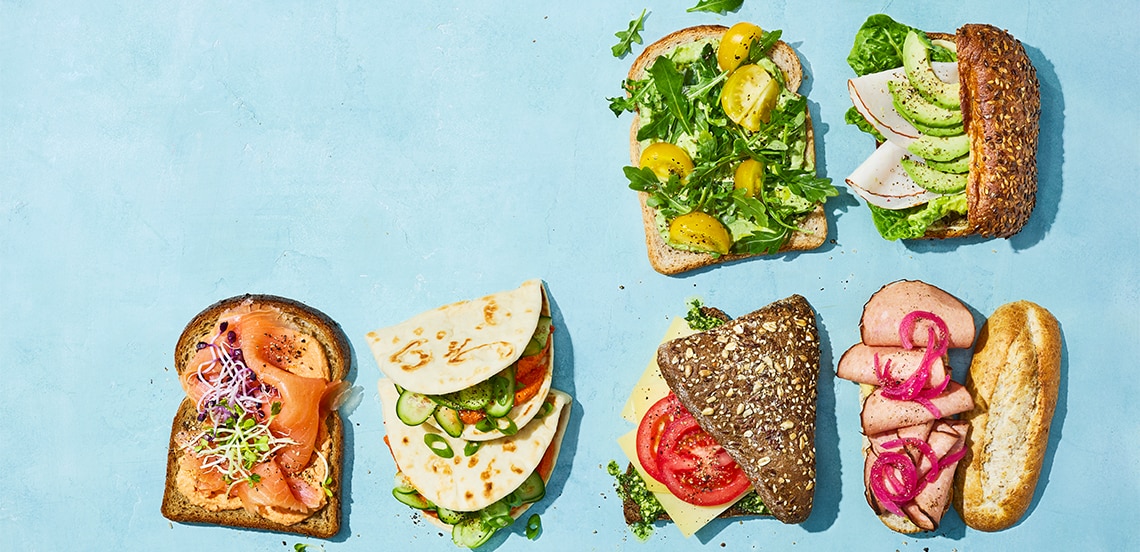 Diverse selectie van belegde broodjes en sandwiches met verschillende toppings zoals zalm, kaas, groenten, avocado, rosbief en gemarineerde ui op een blauwe achtergrond.
