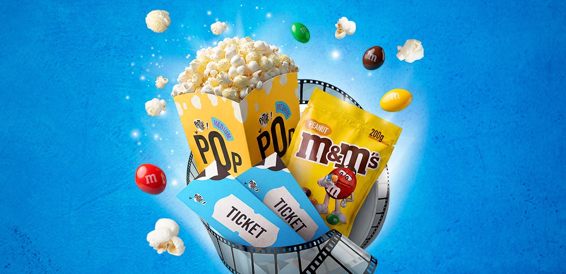 Bak popcorn, zakje M&M's pinda, twee bioscooptickets en filmrol op blauwe achtergrond, met verspreide popcorn en M&M-snoepjes.