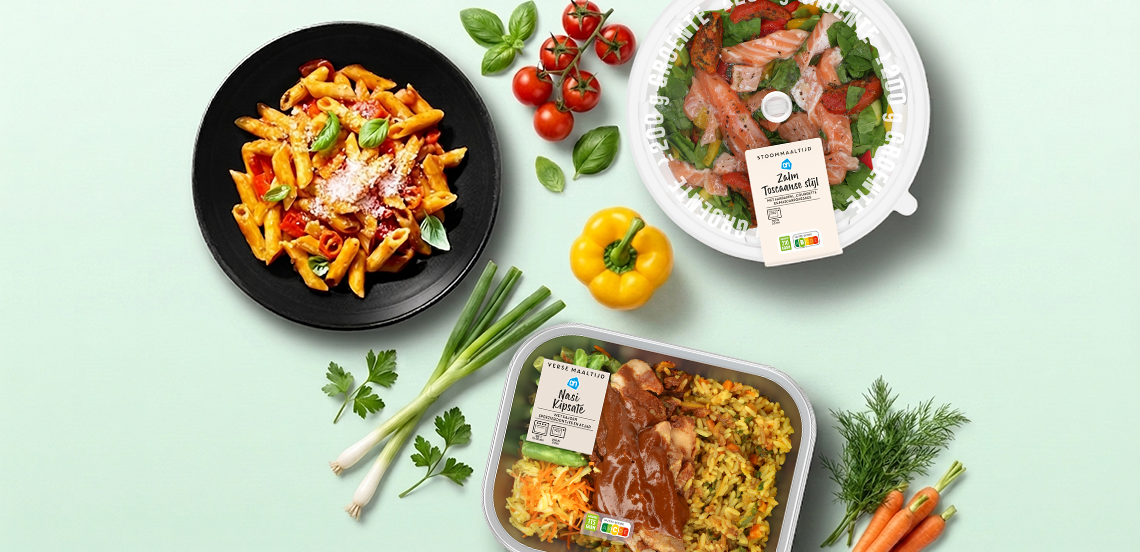 Twee verse kant-en-klaar maaltijden van Albert Heijn, waaronder zalm Toscaanse stijl en nasi kipsaté, met daarnaast een bord pasta, verse groenten zoals cherrytomaten, gele paprika, bosui, basilicum, peterselie en wortels.