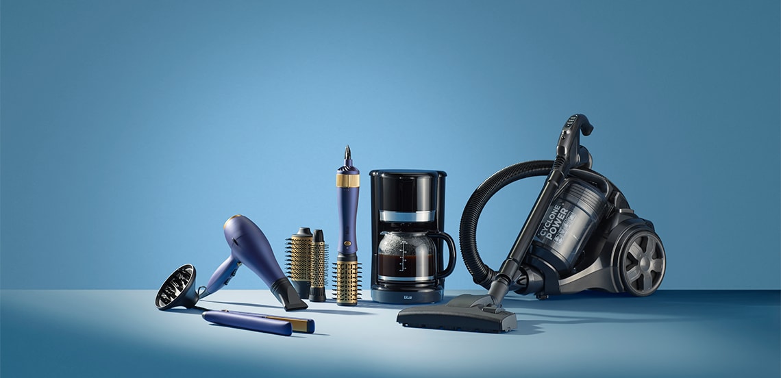 Huishoudelijke apparaten op een rij, waaronder een koffiezetapparaat, een stofzuiger, een föhn, een krulborstel en een stijltang.