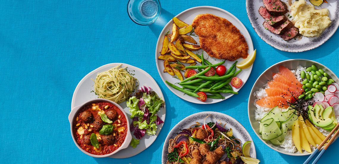 Borden met diverse kleurrijke maaltijden, waaronder schnitzel met aardappeltjes en groenten, pasta met salade, een kom poke bowl met zalm en groenten, oosterse noedels met groenten en vlees, en een bord met gegrild vlees en aardappelpuree, op een blauwe ondergrond.