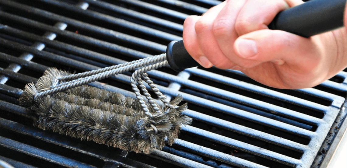 Hand dat een barbecueborstel gebruikt om een grillrooster schoon te maken.