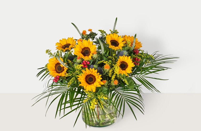 Boeket met gele zonnebloemen en groene bladeren in een glazen vaas