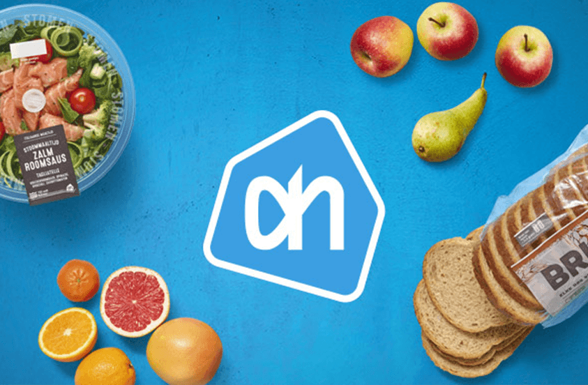 Salade met zalm roomsaus, verschillende soorten fruit, gesneden bruinbrood en het Albert Heijn-logo op een blauwe achtergrond.