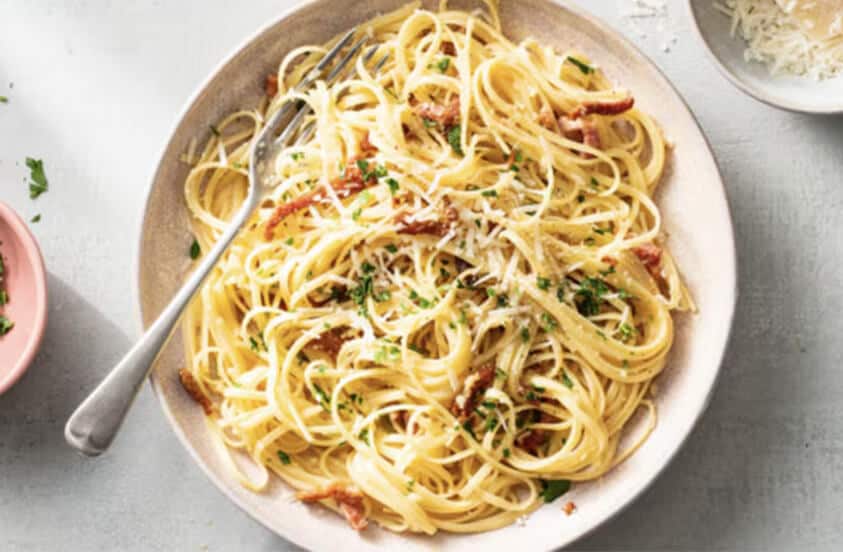 Bord met spaghetti carbonara, bestrooid met geraspte kaas en peterselie.