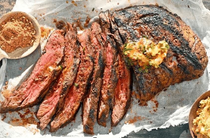 Gegrilde bavette, deels in plakken gesneden en geserveerd met gekruide boter en een kom met droge kruidenrub ernaast.