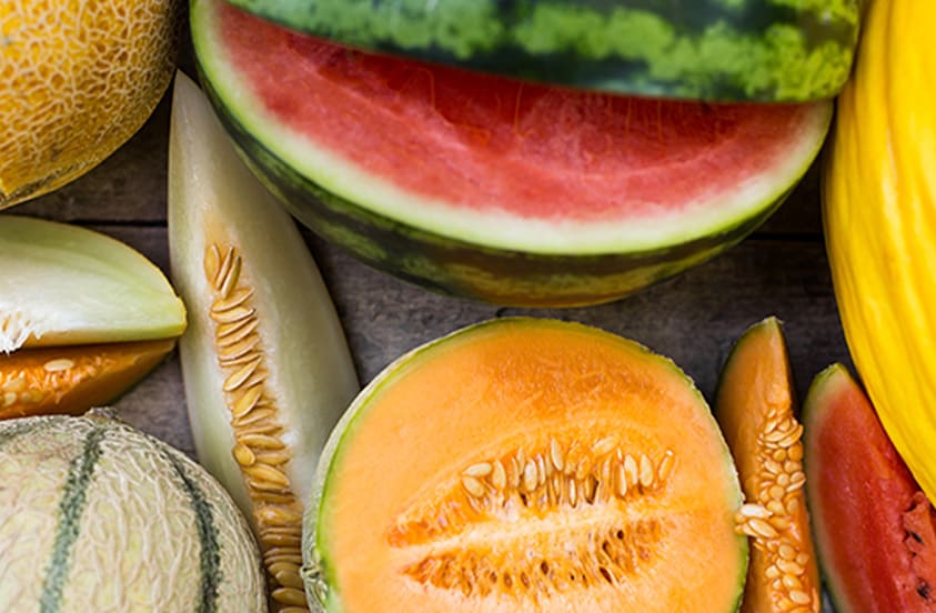 Verschillende soorten gesneden meloenen, waaronder watermeloen, galiameloen, cantaloupe en gele honingmeloen, op een houten ondergrond.