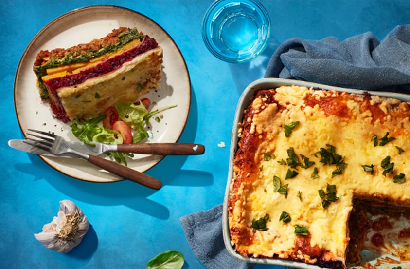 Lasagne in een ovenschaal en een stuk op een bord met bestek.