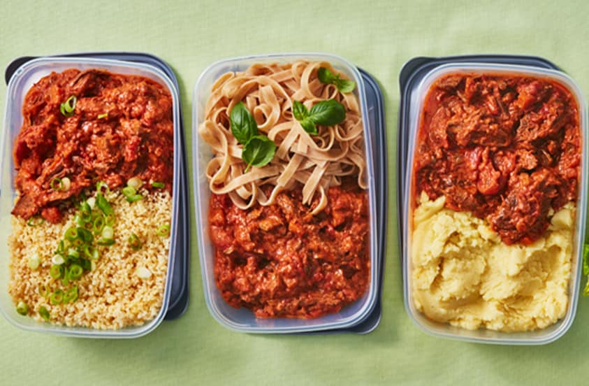 Drie plastic bakjes met maaltijdporties: links bulgur met rundvleesstoof en bosui, in het midden tagliatelle met rundvleesstoof en basilicum, rechts aardappelpuree met rundvleesstoof.