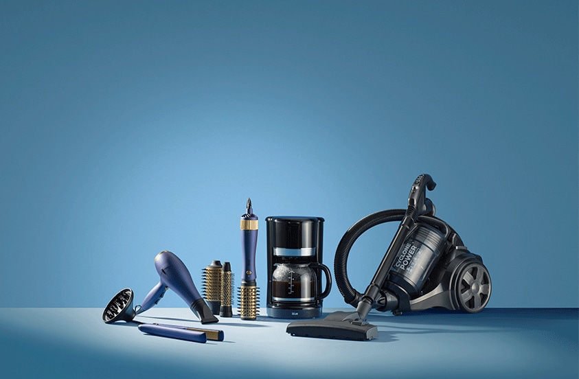 Verschillende huishoudelijke apparaten zoals een föhn, koffiezetapparaat, stofzuiger en haarschikaccessoires op een blauwe achtergrond.