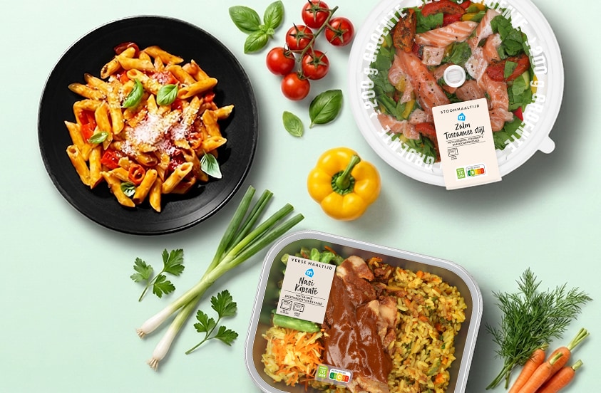 Bovenaanzicht van drie maaltijden: een bord pasta, een ronde schaal met zalm en een maaltijd met rijst, met daaromheen verse groenten en kruiden op een lichtgroene achtergrond.