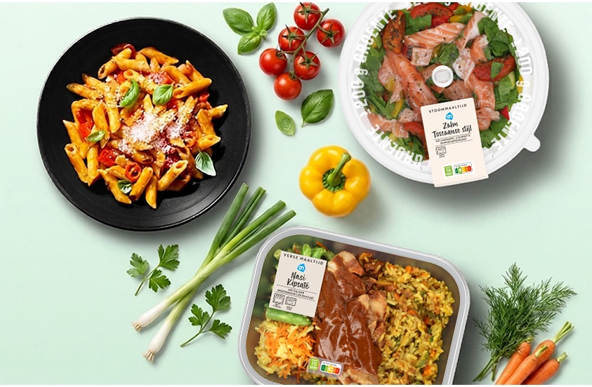 Verse maaltijden van Albert Heijn, waaronder een bord penne pasta met tomatensaus en basilicum, een stoommaaltijd zalm Toscaanse stijl en een maaltijd nasi kipsaté, omringd door verse groenten zoals tomaat, paprika, bosui en wortel.