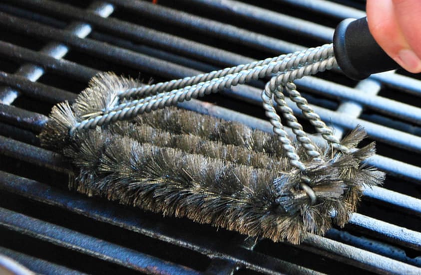 Hand dat een barbecueborstel gebruikt om een grillrooster schoon te maken.