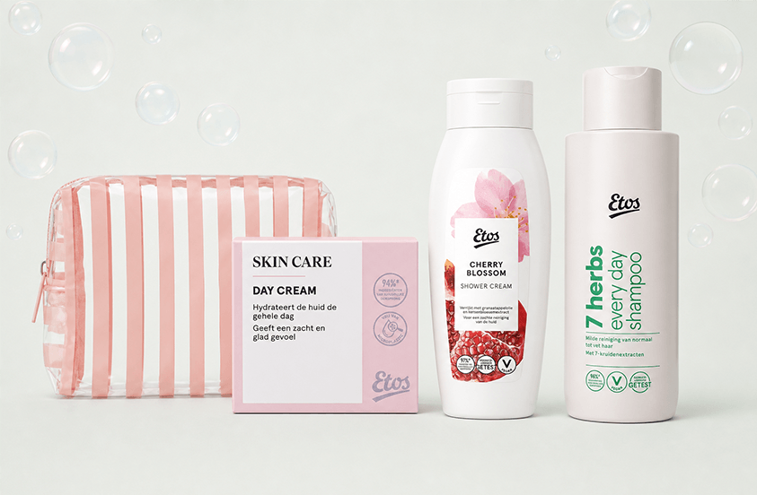 Verzorgingsset met een roze transparant toilettasje, Etos dagcrème, Etos Cherry Blossom shower cream en Etos 7 Herbs Everyday Shampoo, afgebeeld met achtergrond van zeepbellen.