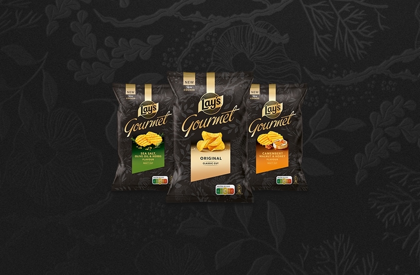 Drie zakken Lay's Gourmet chips in de smaken Original, Sea Salt & Olive Oil Herbs, en Camembert Walnut & Honey tegen een zwarte achtergrond.