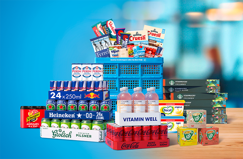 Grote selectie A-merk producten, waaronder Heineken, Grolsch, Red Bull, Schweppes, Peroni, Coca-Cola, Starbucks, Becel, Quaker en Vitamin Well, uitgestald met een blauwe Albert Heijn boodschappenkrat op de achtergrond.