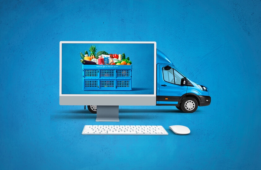 Computer met afbeelding van een blauwe Albert Heijn boodschappenkrat vol boodschappen, op de achtergrond een blauwe bezorgbus, toetsenbord en muis op een blauwe ondergrond