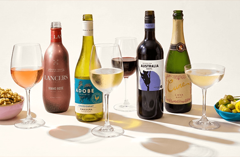 Verschillende flessen wijn, waaronder Lancers rosé, Adobe chardonnay en Cune cava brut, met bijpassende glazen wijn en mousserende wijn, geserveerd naast bakjes met noten en groene olijven.