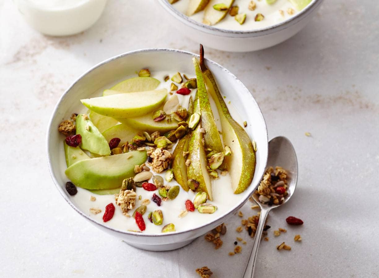 Sojayoghurt ontbijt met pistachenoten, appel, peer, limoen, avocado en granola.