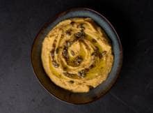 Zoete pompoen laat zich graag in een badje leggen met romige hummus. Daar blijf je in dippen, mee smeren of uit scoopen.