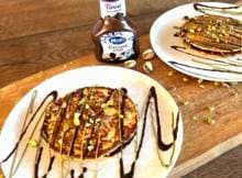 Koken met Hero: Haal de feestdagen in huis met deze feestelijke powerpannenkoekjes met pistache crème, Tova choco drizzle en krokante pistachenoten.  Perfect voor een cozy ontbijt of een lekkere lunch! 